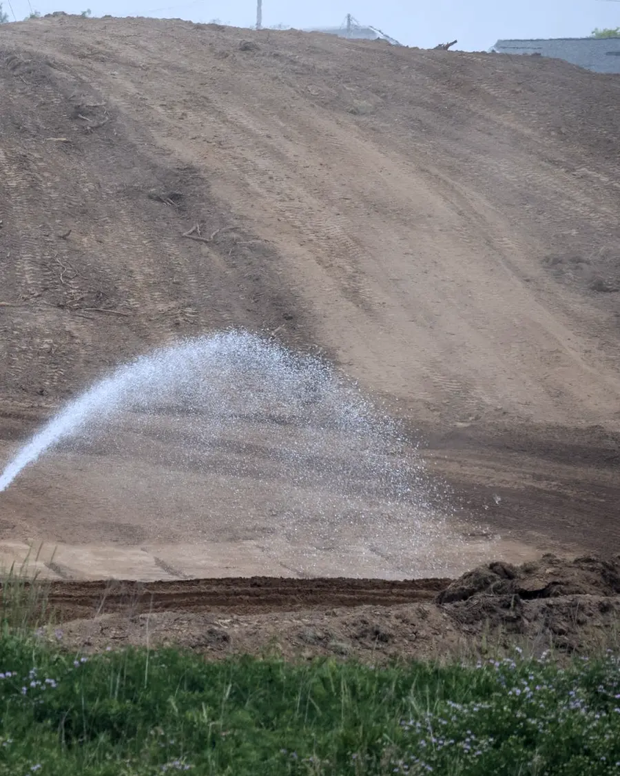 An arc of water landing on a bare earth batter to hold down dust